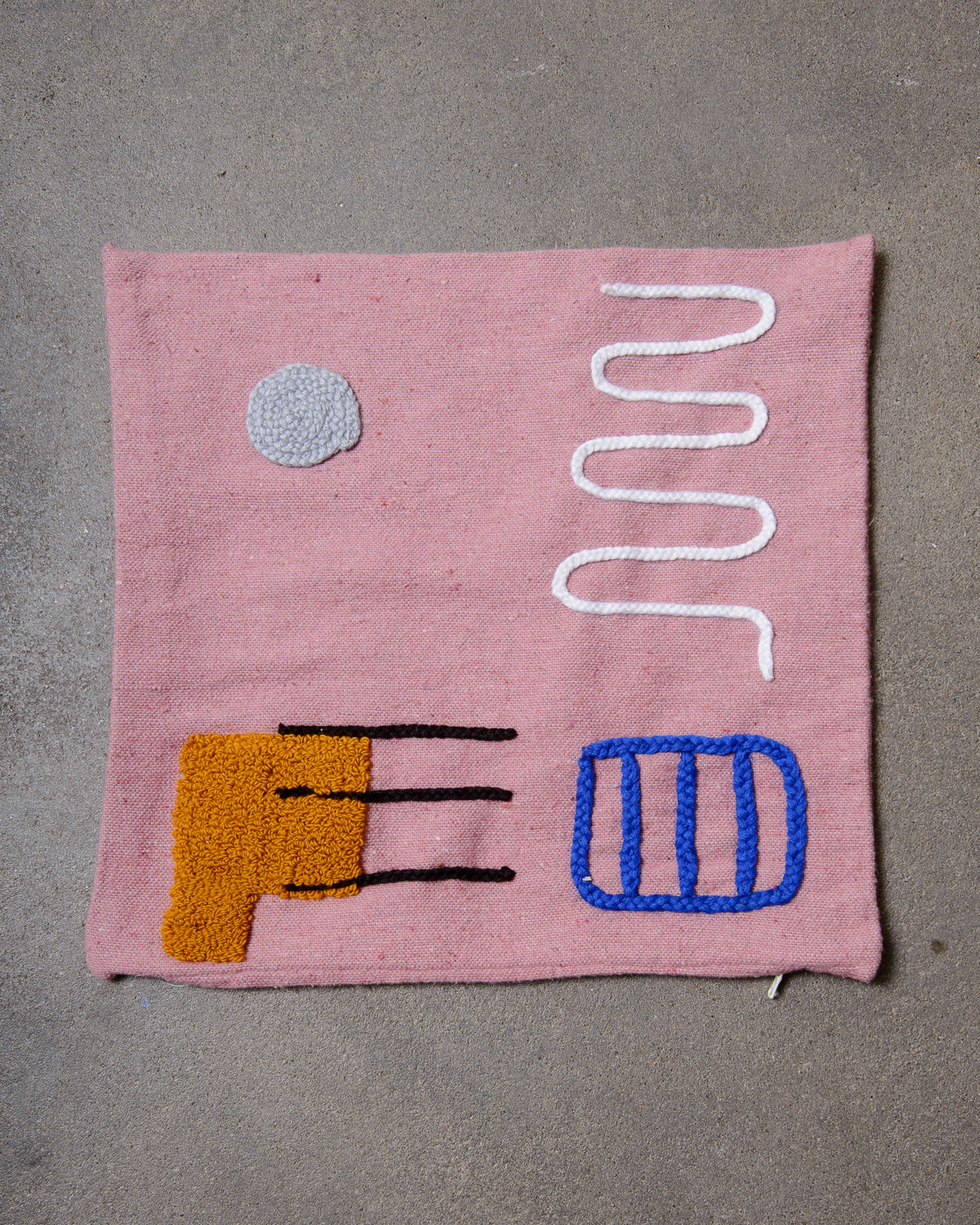Pink cushion cover with hand embroidered abstract design on cement floor.